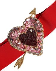 Közeli kép a díszes arany színű szívcsattáról egy Dolce & Gabbana piros széles övén, az olasz kézművesség bemutatásával.