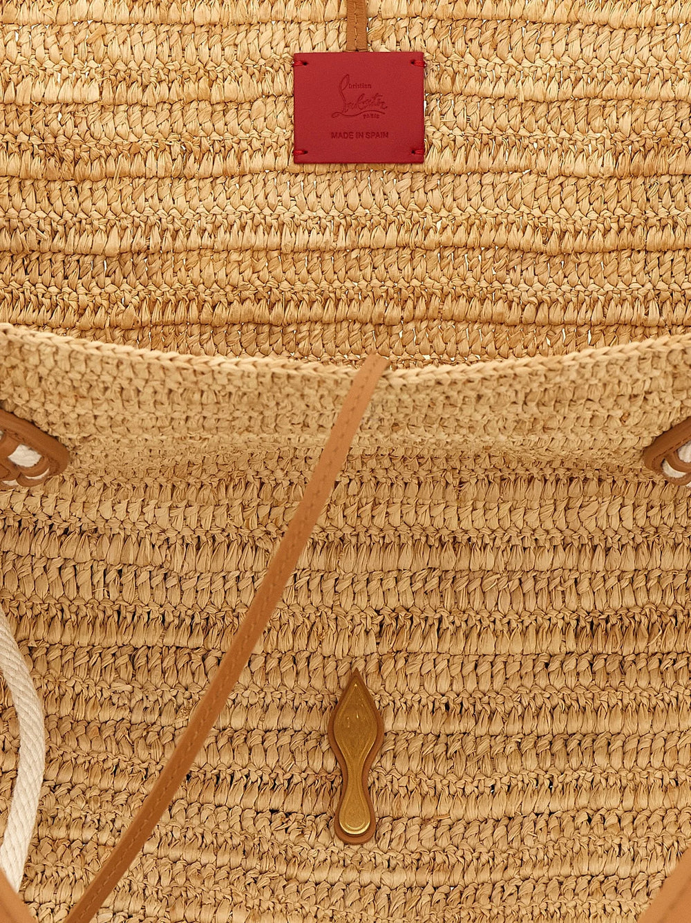 Detailní pohled na tote tašku Christian Louboutin, zdůrazňující složitý proplet rafie a prvotřídní cervené kožené prošívání.