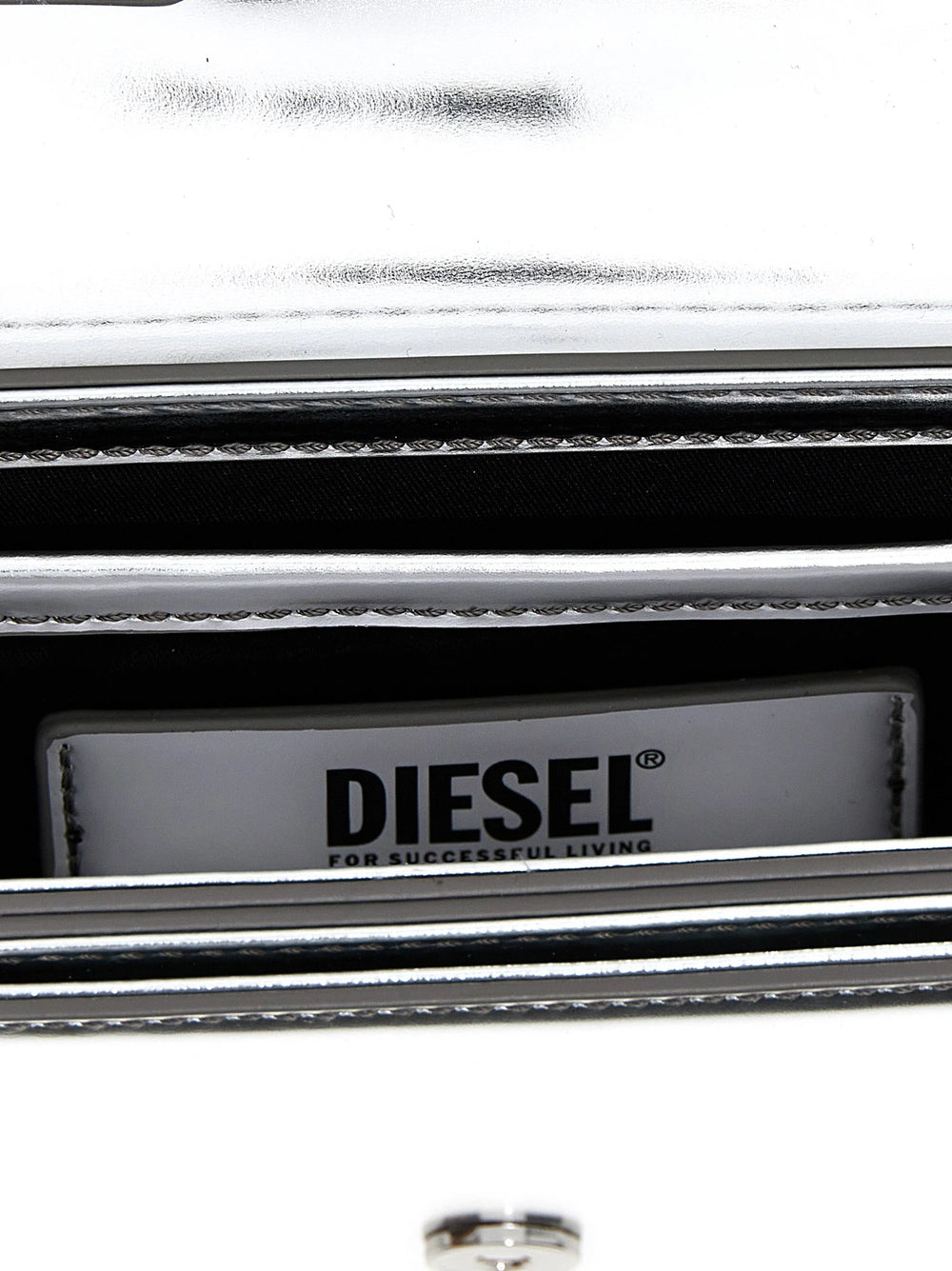 Detailny pohľad na striebornu ramennu kabelku Diesel ukazujúci texturu kravskej usne a leštene kovove prvky.