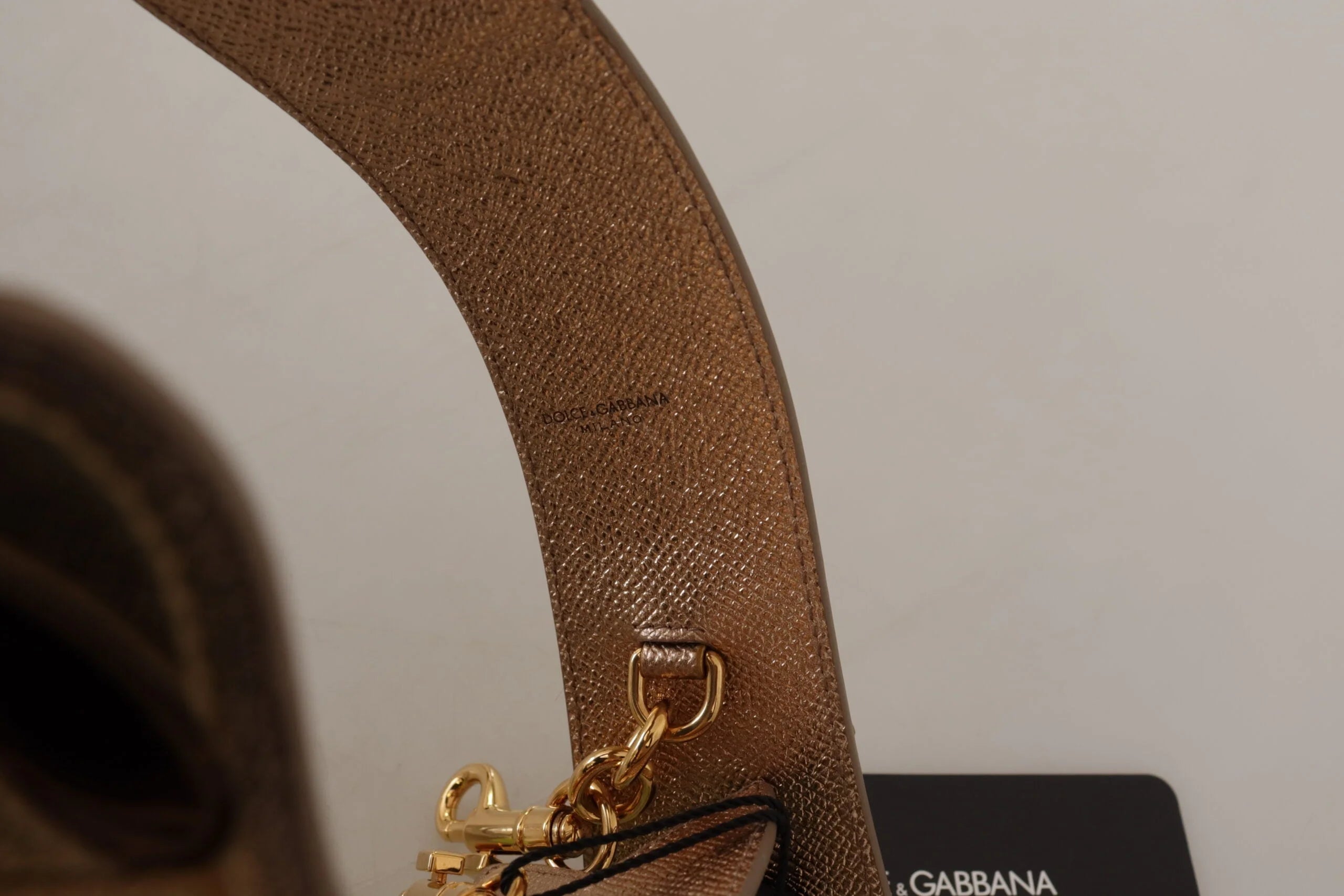 Dolce & Gabbanan metallinhohtavan kultaisen nahka-lisäkkeen takapuoli, jossa on sileä vuori ja kullanväriset yksityiskohdat.