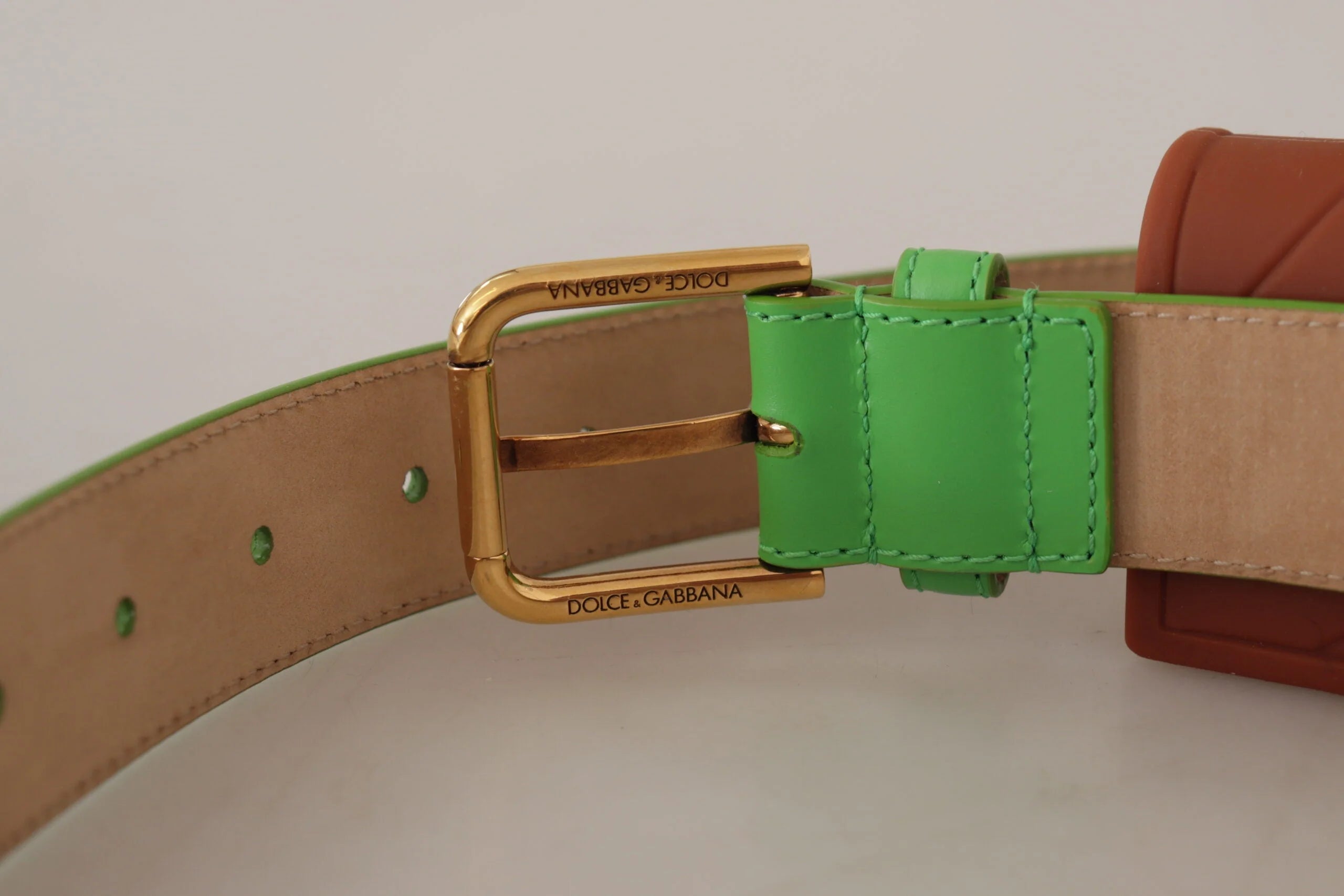 Détail de l'emblème Devotion en cœur doré sur l'attache en cuir vert pour micro sac.