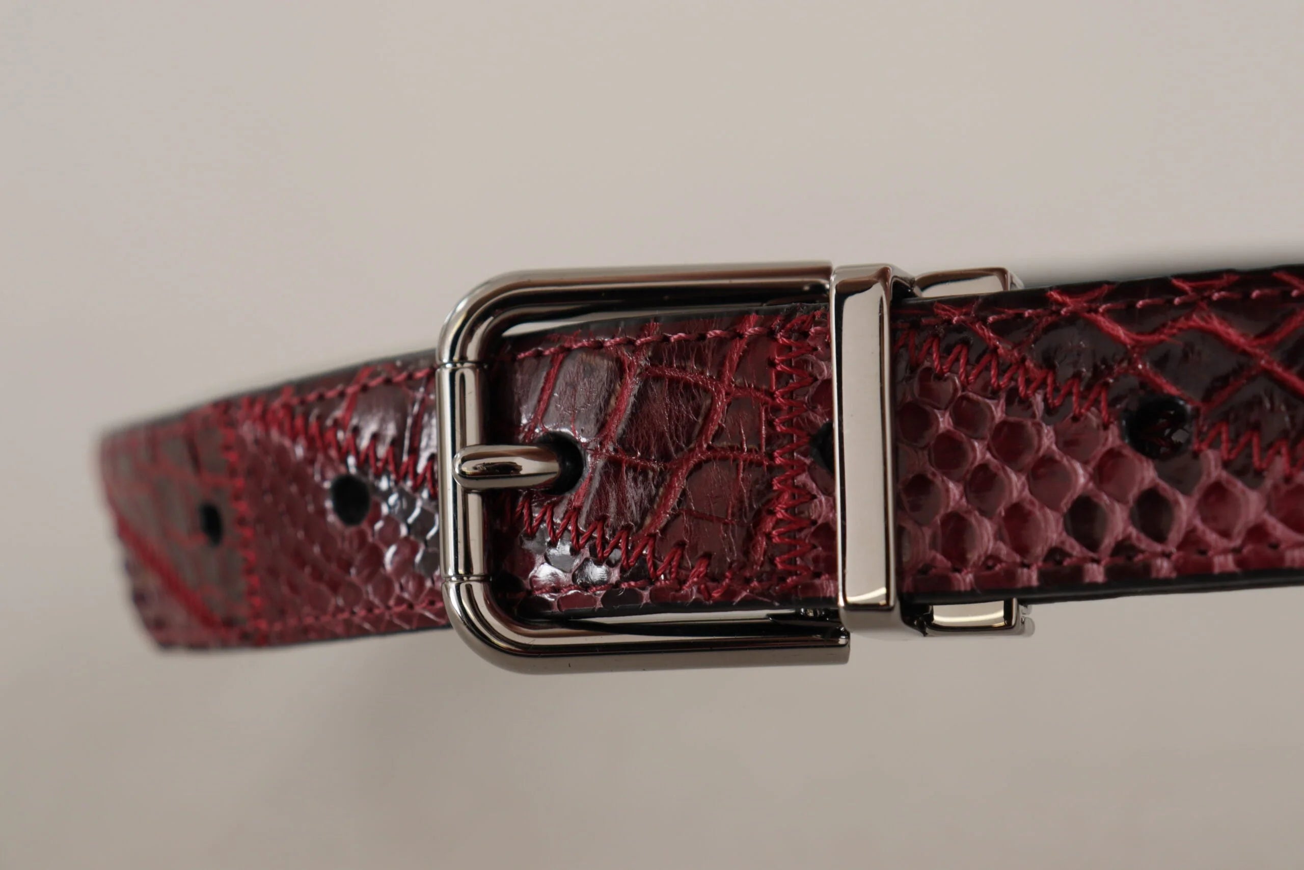 Detailní záběr na ikonické zlaté logo DG na červeném pythoním pásku, odrážející řemeslnou zručnost Dolce & Gabbana.
