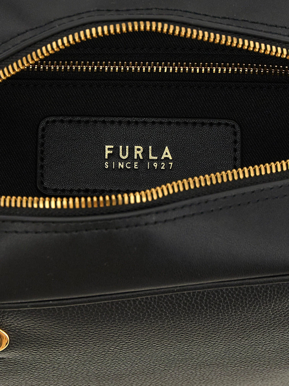 Detalhe close-up da mala Furla, mostrando a grão de couro de bezerro premium e o fecho metálico polido com o logótipo.