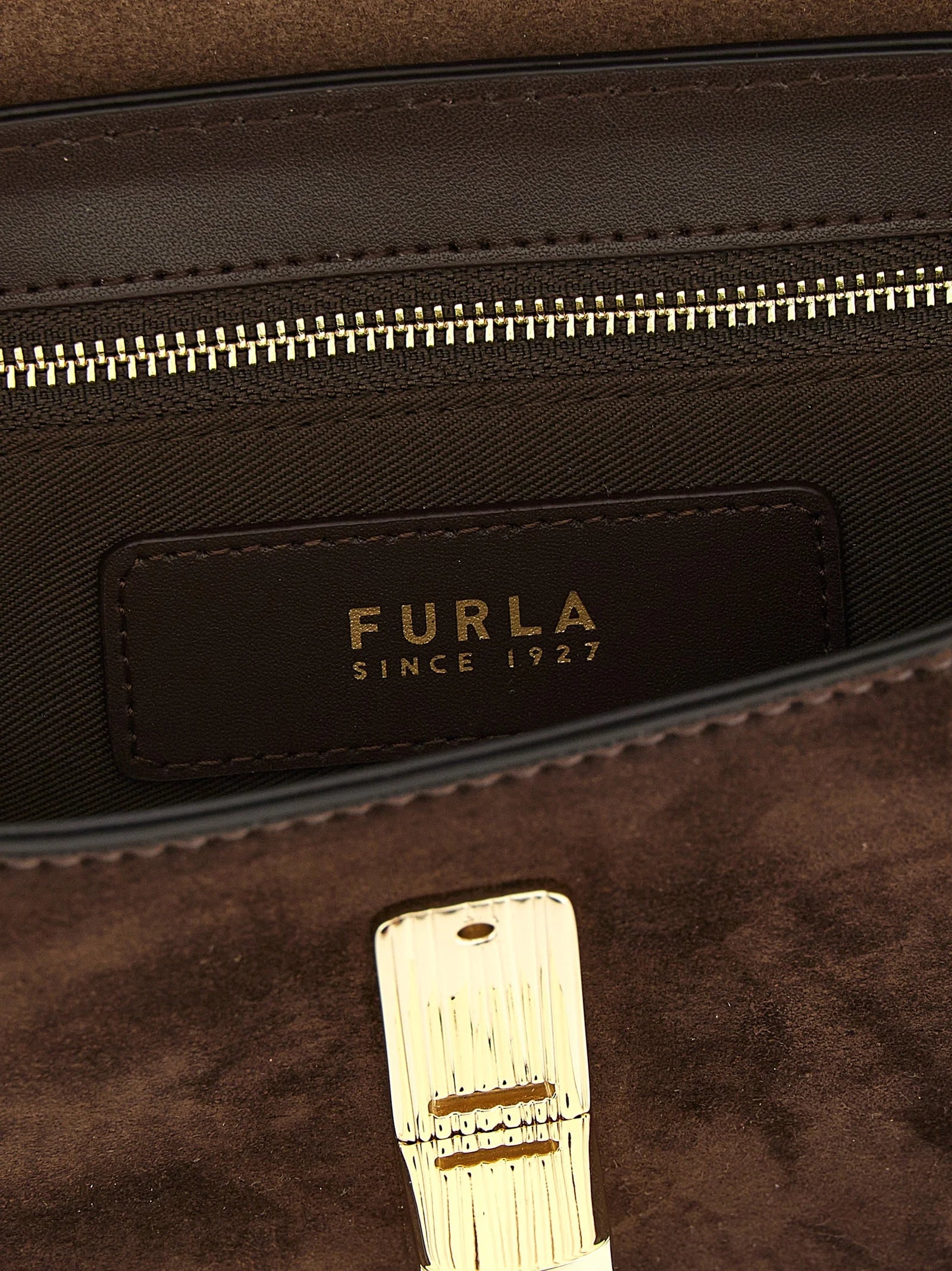 Detailní pohled na gravírování loga Furla a jemnou strukturu prémiové hnědé hovězí kůže.