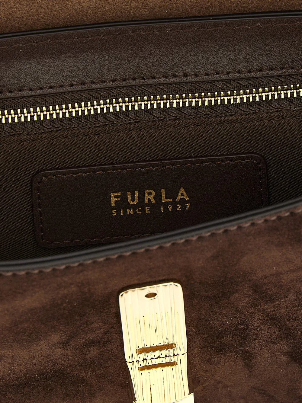Detailní pohled na gravírování loga Furla a jemnou strukturu prémiové hnědé hovězí kůže.