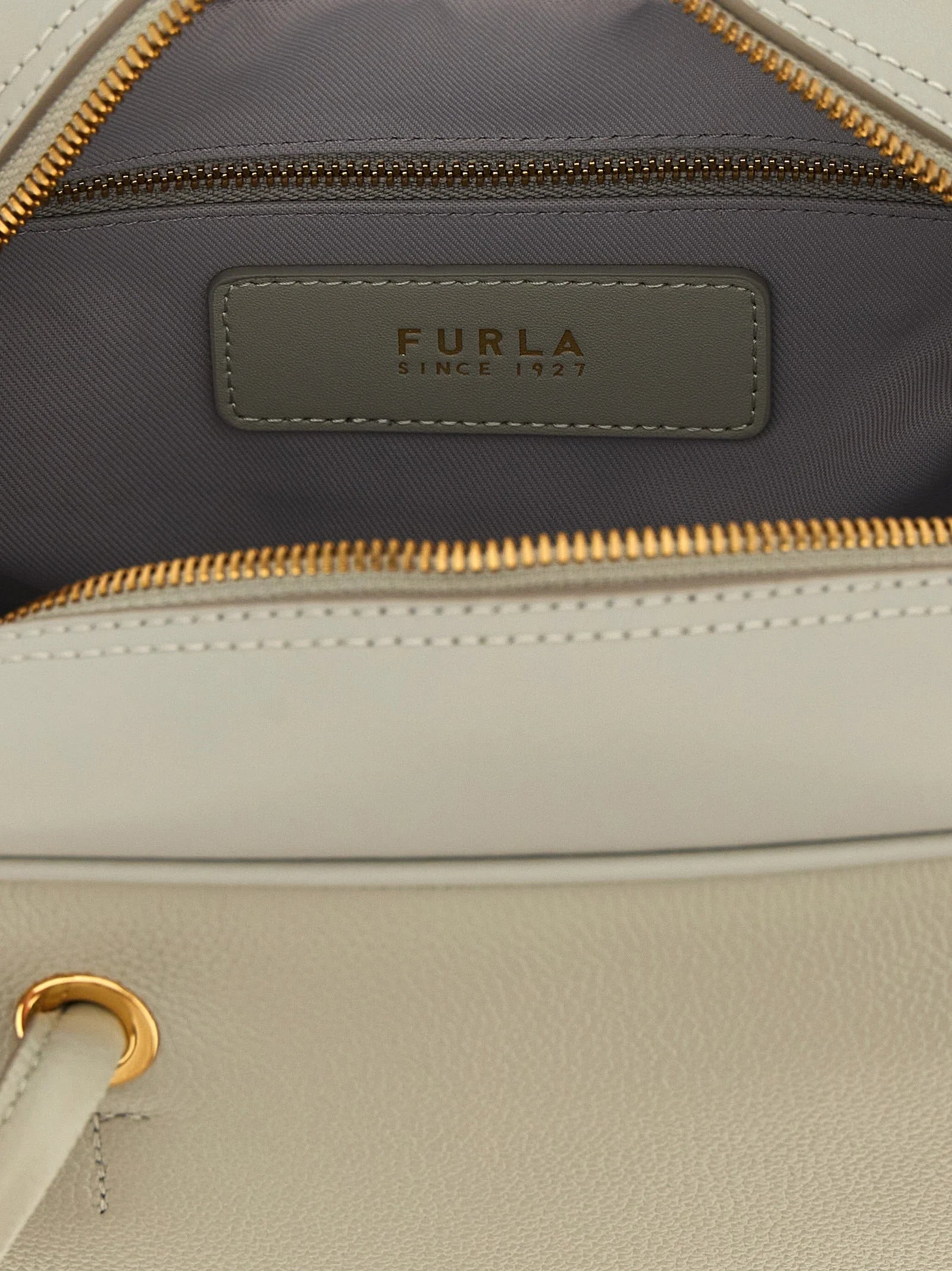 Zbliżenie na torebkę Furla w kolorze szarym, ukazujące drobne ziarno wysokiej jakości skóry cielęcej i polerowane elementy metalowe.