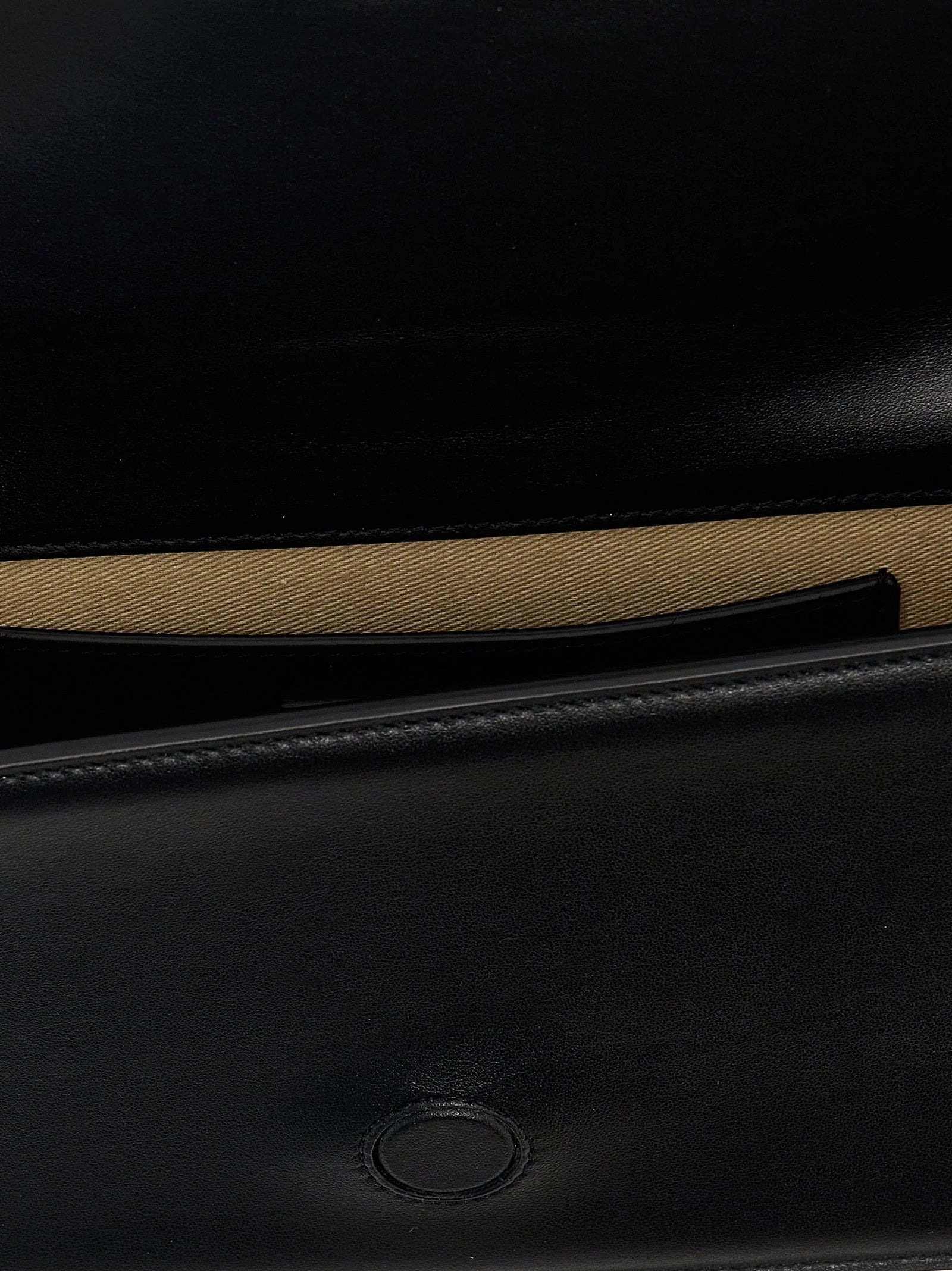 Close-up of the Jacquemus gold-tone metal logo lettering on premium black cowhide leather grain.
