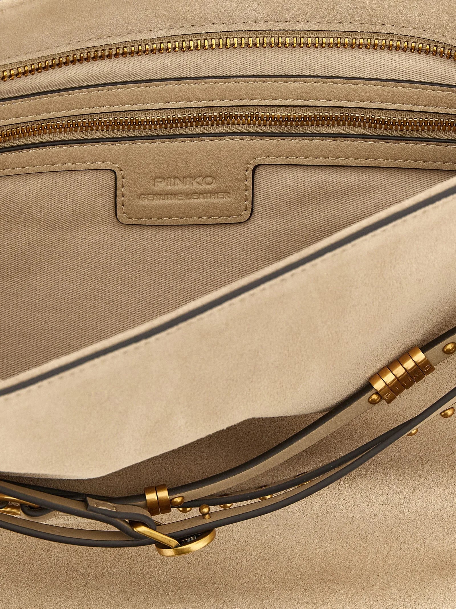 Dettaglio a figura intera della ferramenta dorata PINKO e della pregiata pelle di vacchetta sulla borsa a tracolla beige.