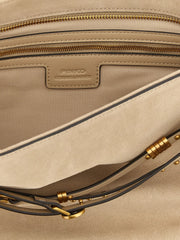 Dettaglio a figura intera della ferramenta dorata PINKO e della pregiata pelle di vacchetta sulla borsa a tracolla beige.